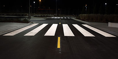 Highly visible pavement markings, including crosswalk and lane dividing line, at night.
