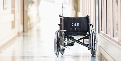 An empty wheelchair waits in a brightly lit hospital hallway.
