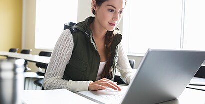 A female student works on a laptop near a bright sunny window, and 3M™ Window Films reduce the glare on her computer screen.
