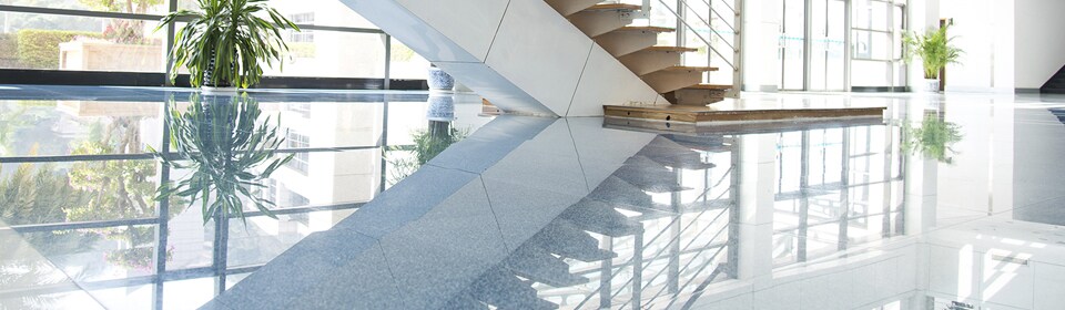 Image of room with staircase reflected in highly polished stone floors
