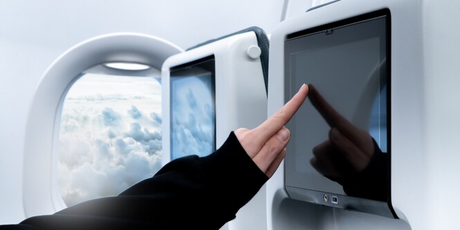 Persona en un avión tocando la pantalla multimedia del respaldo del asiento de enfrente.
