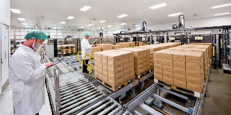 Imagen de trabajadores con mascarilla en una sala blanca limpia, verificando pilas de paquetes.

