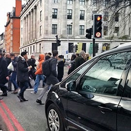 Crowded crosswalk in urban area with car waiting at stoplight.
