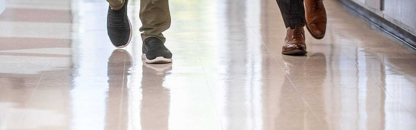 Two pairs of shoes walking on a highly polished floor.
