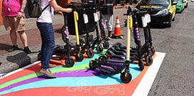 Colorful painted pavement for scooter parking on urban road, with scooters and person holding handlebars of scooter.
