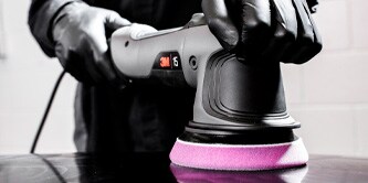 Persona opera una pulidora roto orbital 3M con una borla de pulido purpura sobre una superficie automotriz.
