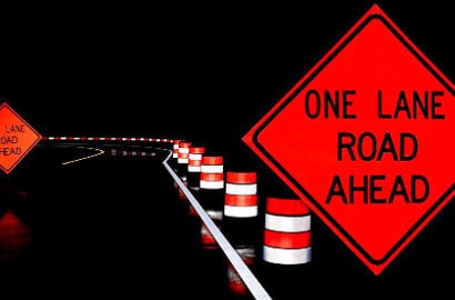 Road sign and cones on wet road at night.