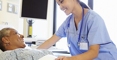 Healing sunlight streams through the window as a female nurse in blue scrubs tends to a patient.
