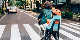 Adult riding bicycle with small child in child seat on urban road near crosswalk.
