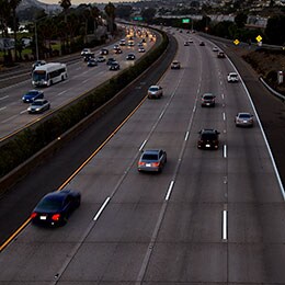 A busy eight-lane highway at dusk has easily viewable pavement markings.