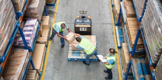 Vista aérea de trabajadores transfiriendo cajas de un pallet a una estantería.
