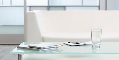 3MTM Glass Finishes cover windows in a hotel lobby where a white couch and newspapers invite travelers to rest.
