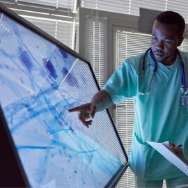 Un profesional de la medicina señalando una gran pantalla en la que se muestran resultados médicos. 