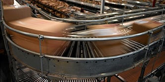 Imagen de cajas desenfocadas moviéndose rápidamente en una curva en un sistema de cinta transportadora.
